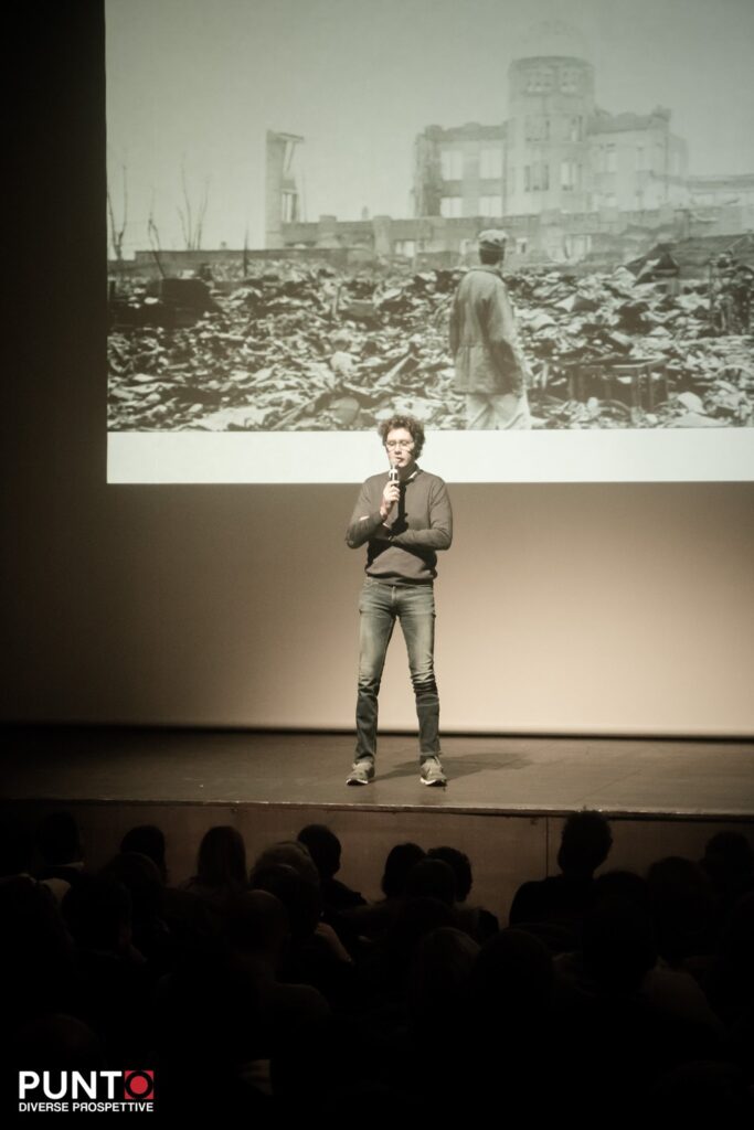 Bernardo sul palco di Punto diverse prospettive mentre paragona la devastazione provocata da un incidente traumatico alla devastazione lasciata dalla guerra